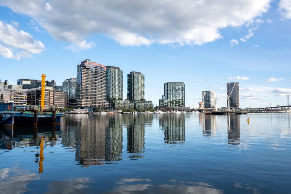 A cluster of modern high-rise office buildings and residential towers against a clear blue sky in an urban cityscape. The buildings feature various materials including glass and concrete, with reflect